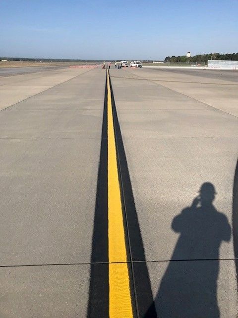 Runway with double yellow centerline stretching into the distance, with a person’s shadow in the foreground.