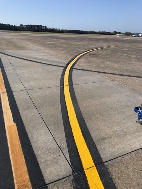 Airport taxiway with curved yellow and black centerline markings on concrete pavement.