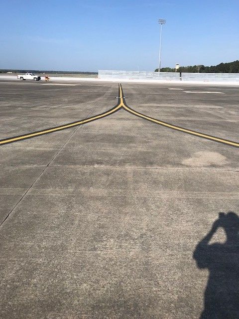 Airport runway with yellow taxiway lines and a distant aircraft under a clear sky