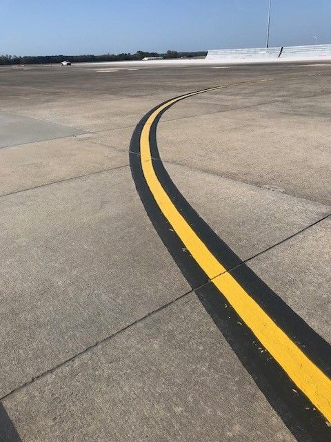 Airport tarmac with a curved yellow taxiway line on concrete pavement, blue sky in the distance