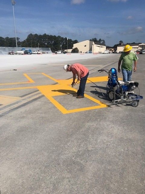 Workers painting yellow parking lines on a rooftop lot, with tools and equipment nearby.