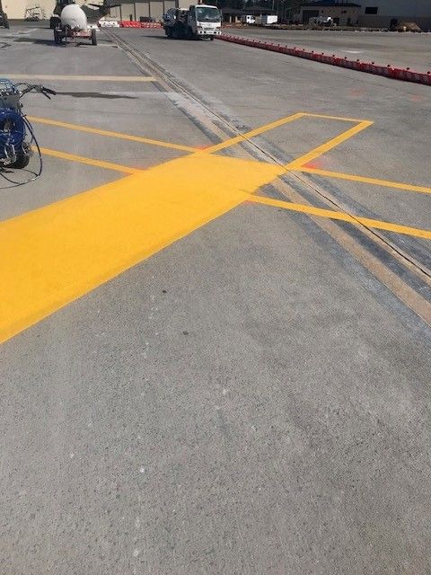 Yellow painted markings on a gray parking lot, with a curb and a bicycle at the left edge.