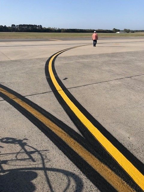 Airport runway with curved yellow and black taxiway lines and a person walking in the distance.