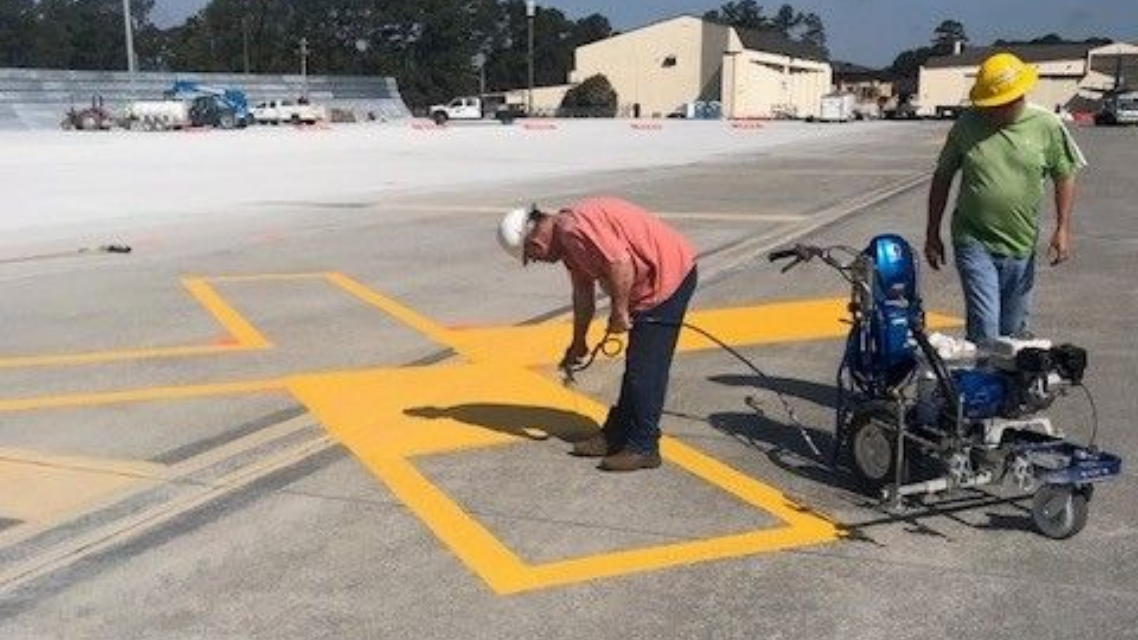 Workers painting yellow markings on an asphalt surface next to a wheelchair and equipment