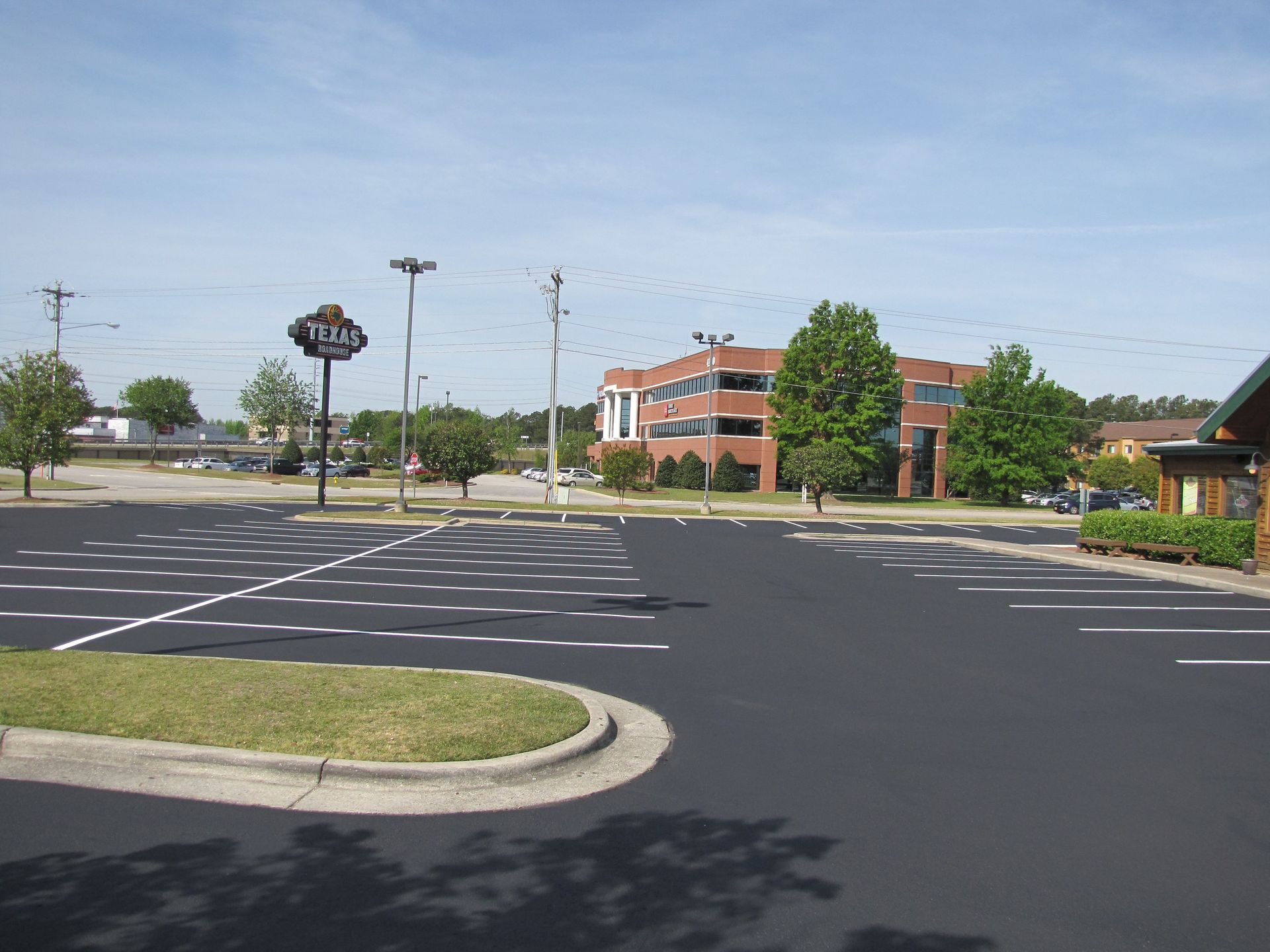 Empty parking lot with a brick office building and trees on a sunny day