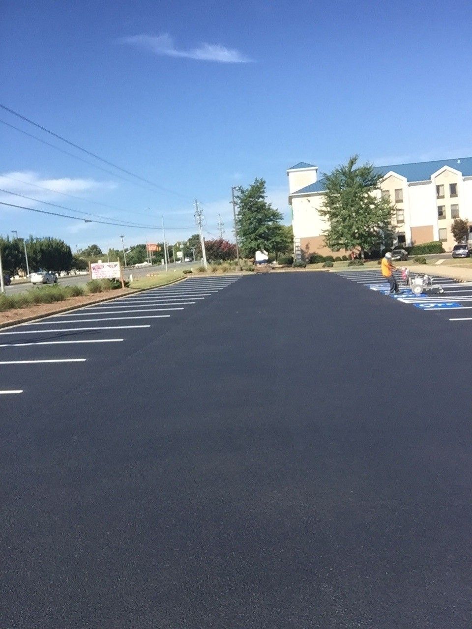 Empty parking lot with fresh black asphalt, white parking lines, and a building in the background