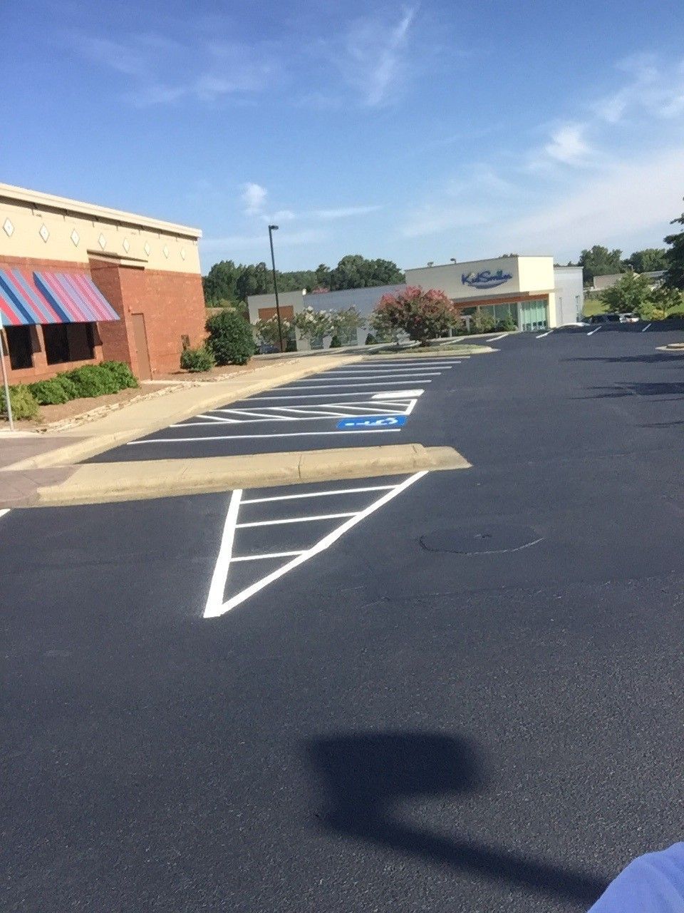 Empty parking lot with painted crosswalk, storefronts, and blue sky
