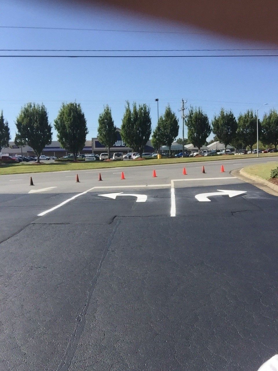 Empty road with white turn arrows, orange cones, and trees under a clear blue sky.