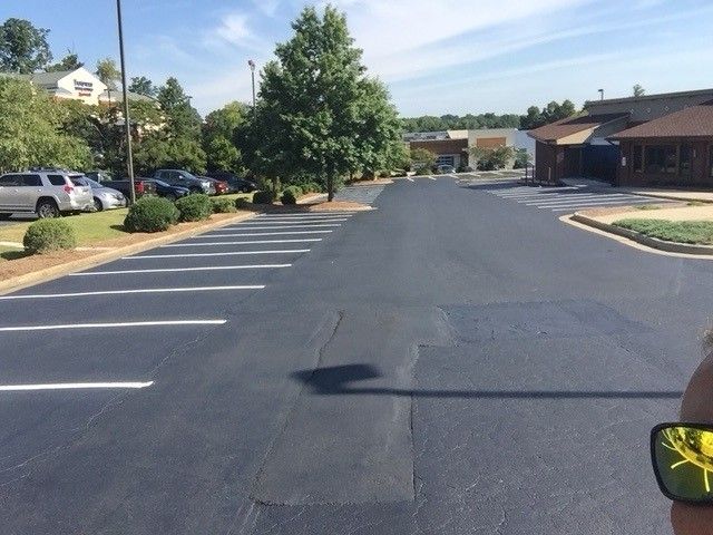 Parking lot with lined spaces, trees, cars, and buildings on a sunny day