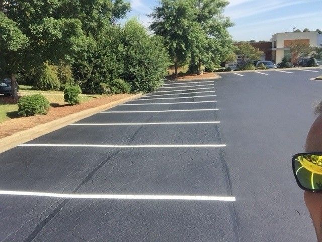 Empty parking lot with white-striped spaces, trees on the left, and a partial person at right edge.