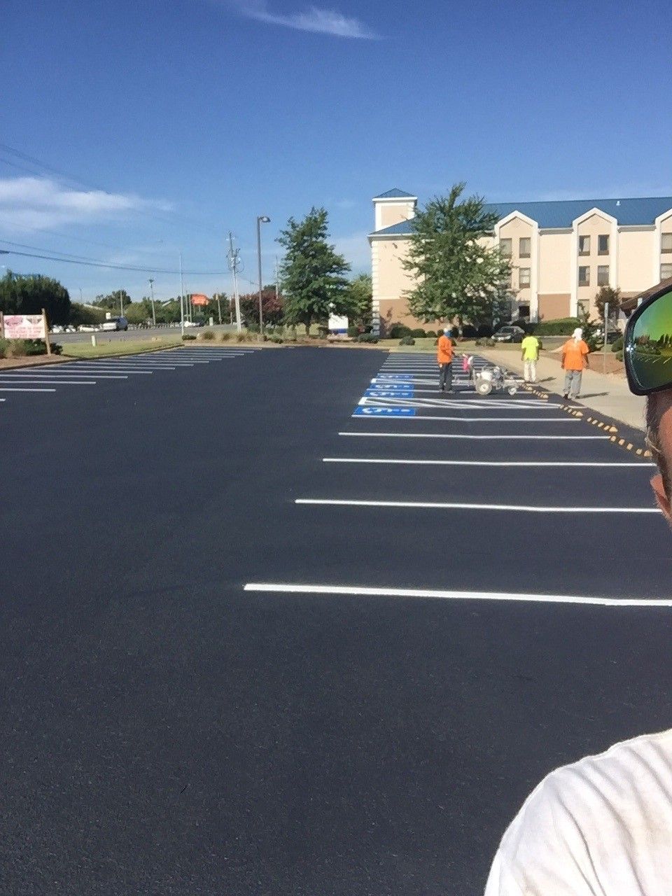 Freshly paved parking lot with white lines, blue handicap spaces, and workers near a beige building