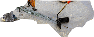 A worker uses a handheld tool to apply sealant to a crack in a paved surface.