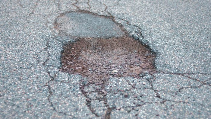 A deep, irregular pothole in asphalt pavement surrounded by a network of surface cracks.