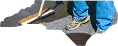 A person in blue jeans uses a push broom to spread a dark liquid sealant over an asphalt surface shaped like North Carolina.