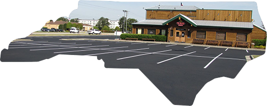 A wood-sided restaurant building with a large, paved parking lot in the foreground, shaped like North Carolina.
