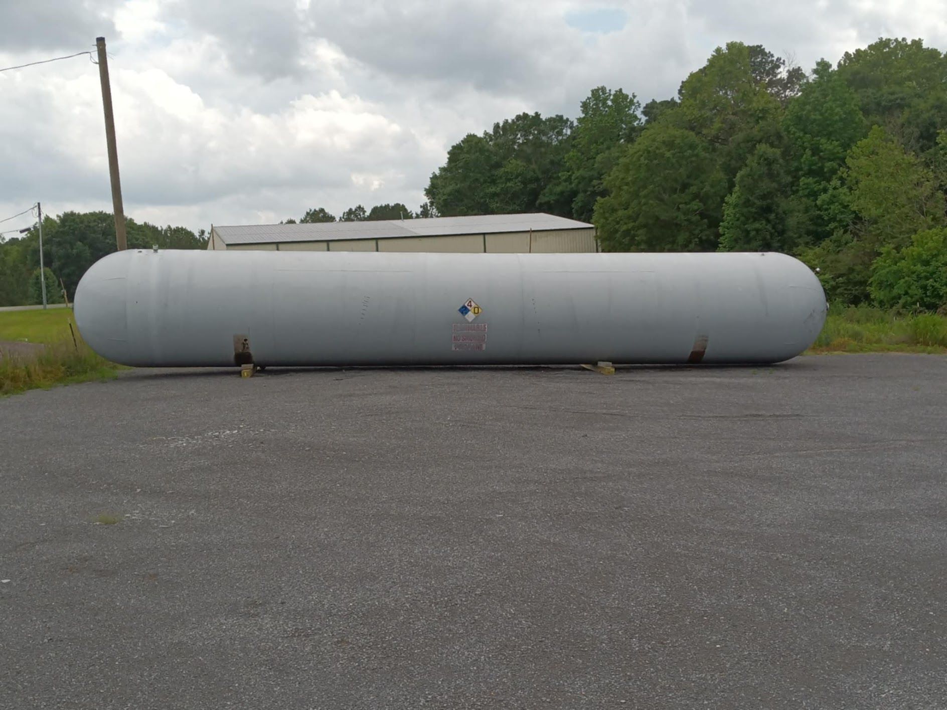 Long, gray industrial propane tank on concrete, outdoors.