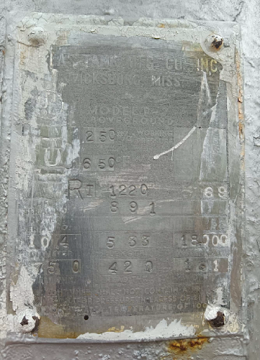 Metallic equipment plate with embossed text, possibly a model or serial number, on a weathered surface.