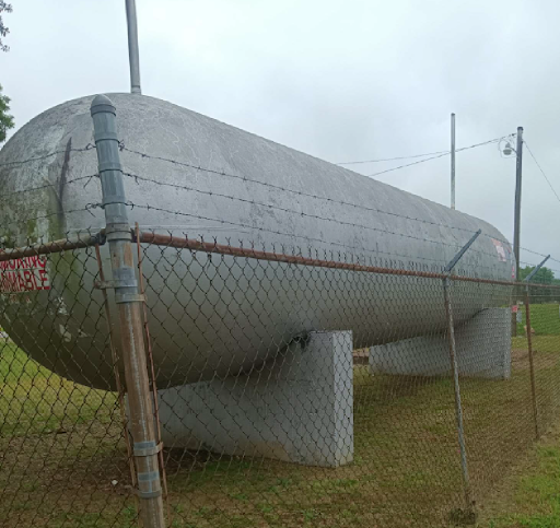 Large, gray, horizontal propane tank behind a chain-link fence.
