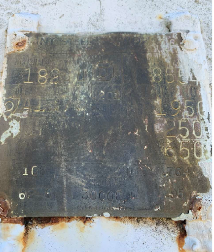 Close-up of a weathered, rectangular stone plaque with engraved numbers and letters, mounted on a white surface with rust.