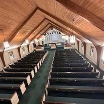 The inside of a church with rows of benches and a wooden ceiling.