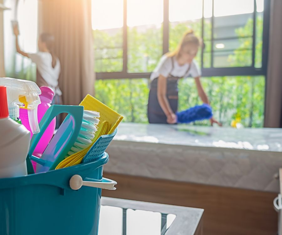A woman is cleaning a window with a mop and a bucket of cleaning supplies.