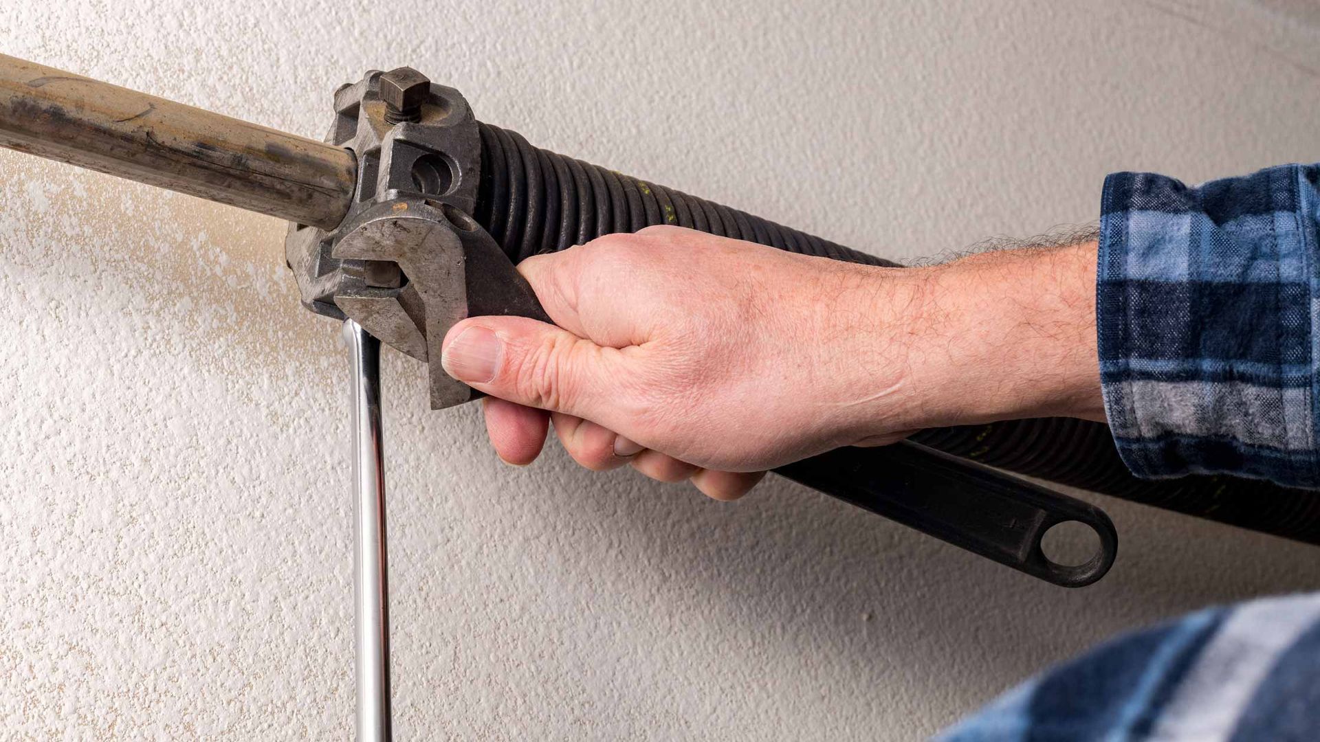 Hand tightening a pipe with a large wrench against a wall-mounted pipe.