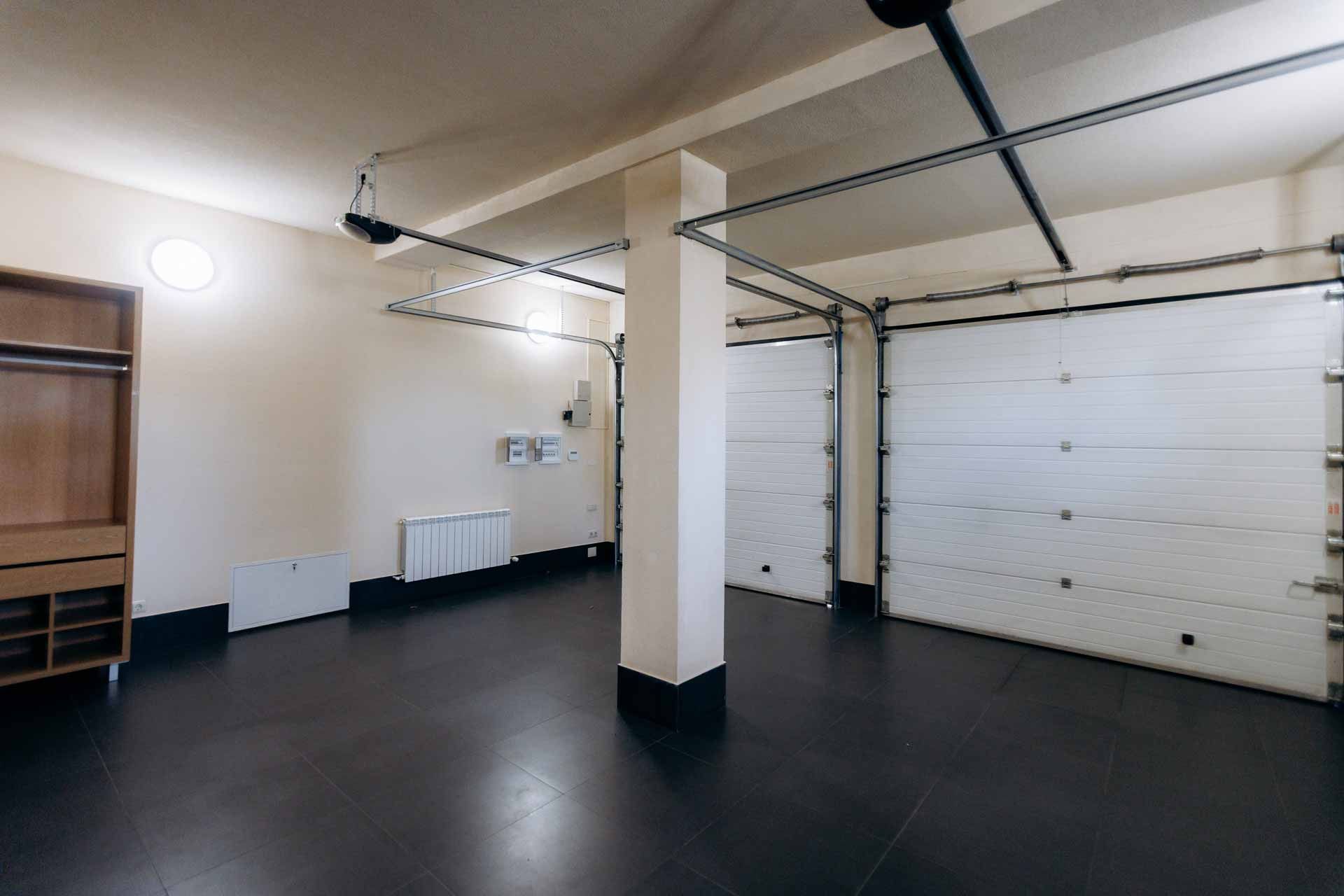 Empty garage interior with white walls, black floor, and closed white garage door