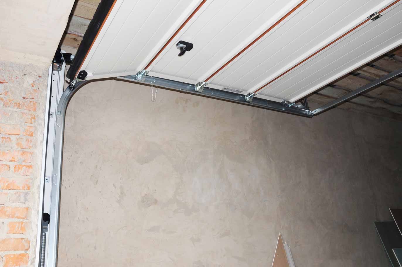 Partially installed garage door with white panels and metal tracks above a bare wall
