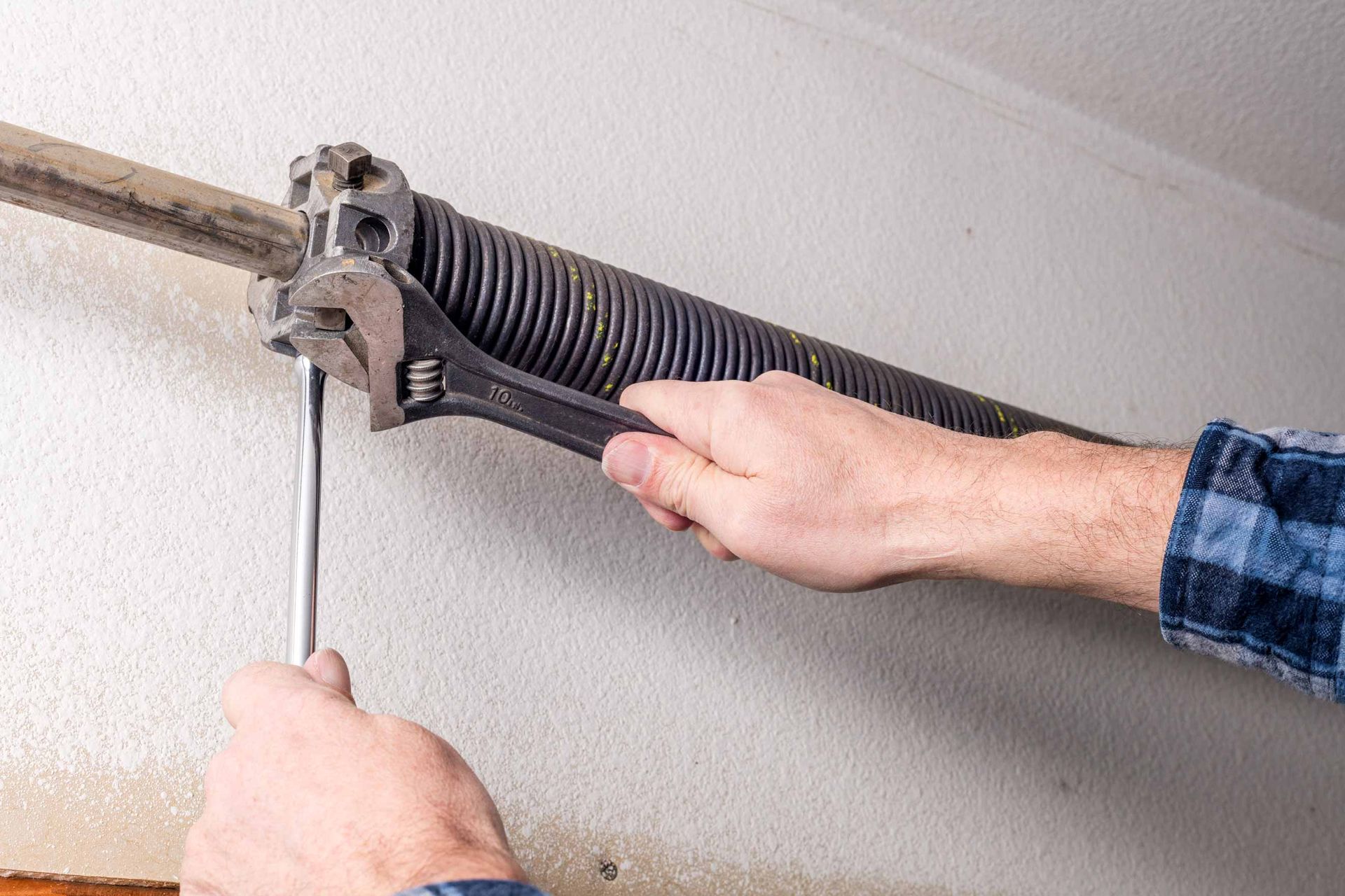 Hands adjusting a black torsion spring on a garage door track with a screwdriver