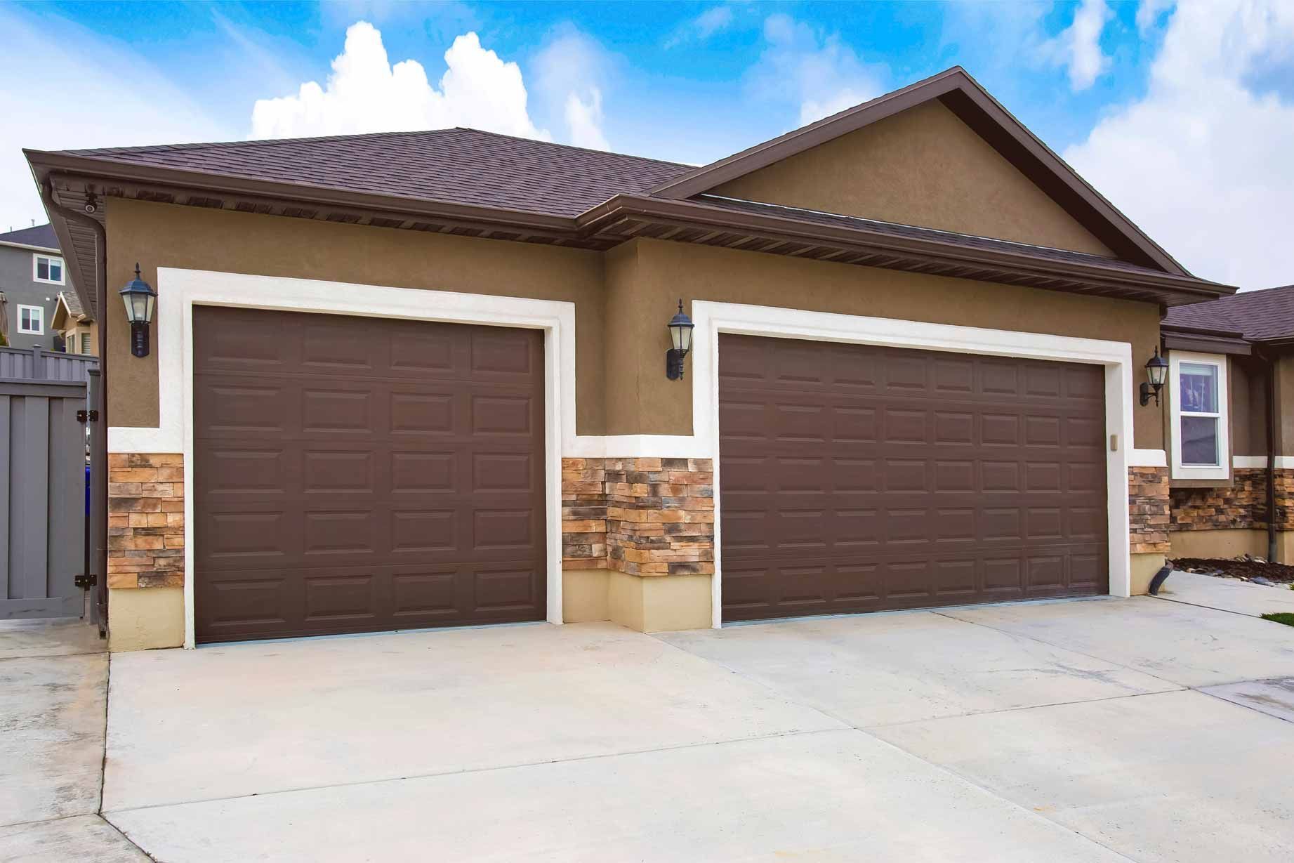 Two brown garage doors on a tan suburban house with stone accents and a concrete driveway