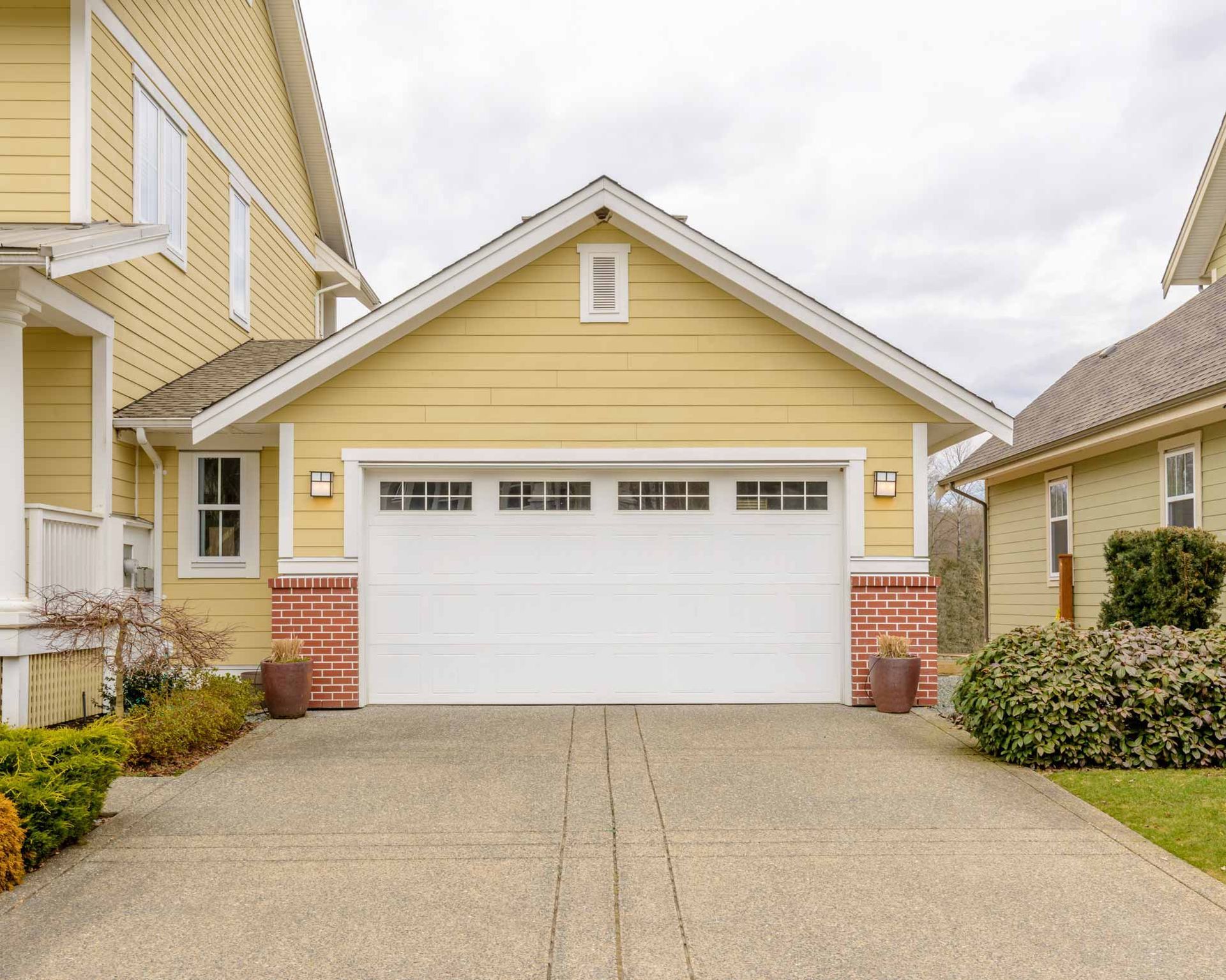 Yellow suburban house with white garage door, brick accents, and a concrete driveway
