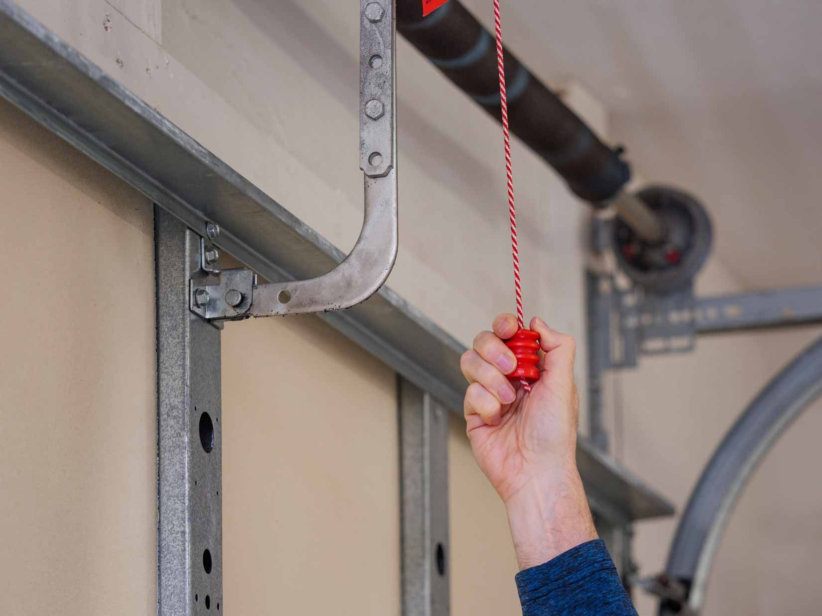 Hand holding a red pull cord in a garage beside metal door tracks