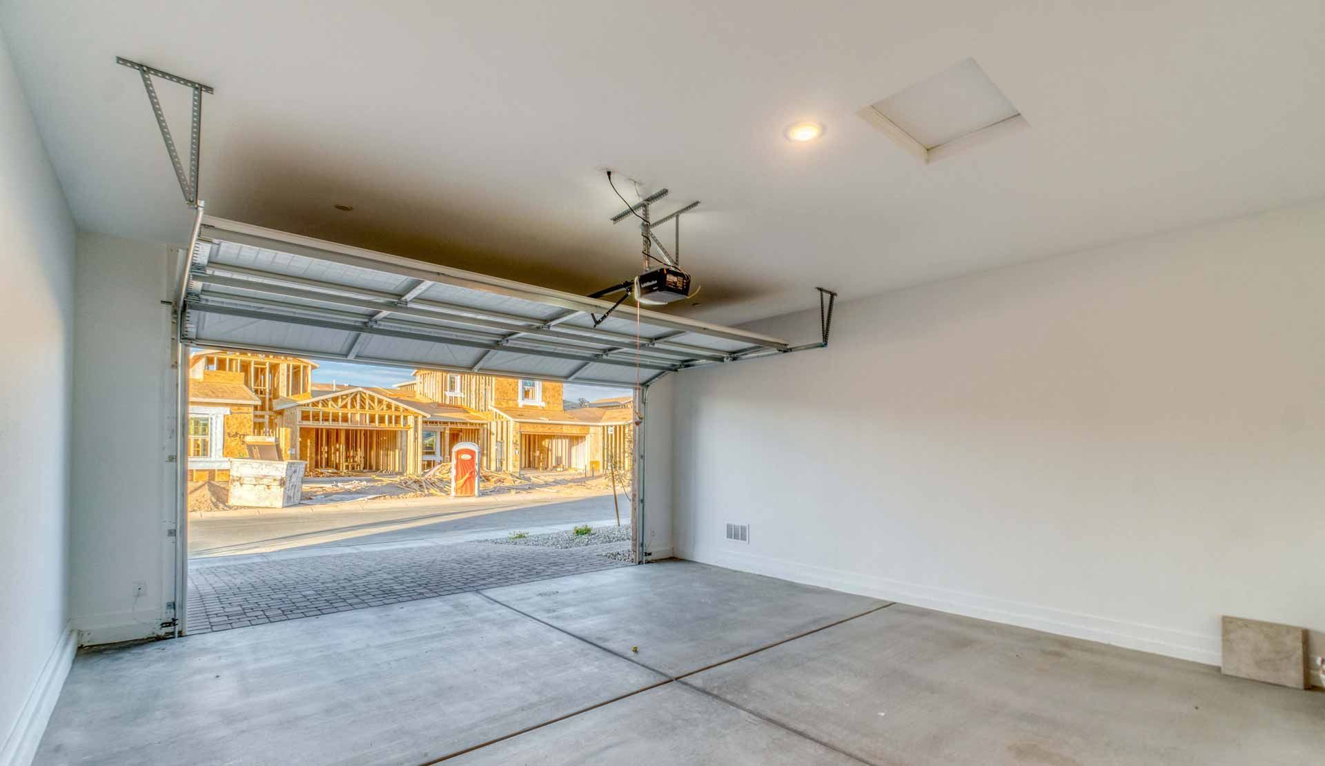 Empty garage interior with open door, concrete floor, and view of houses outside
