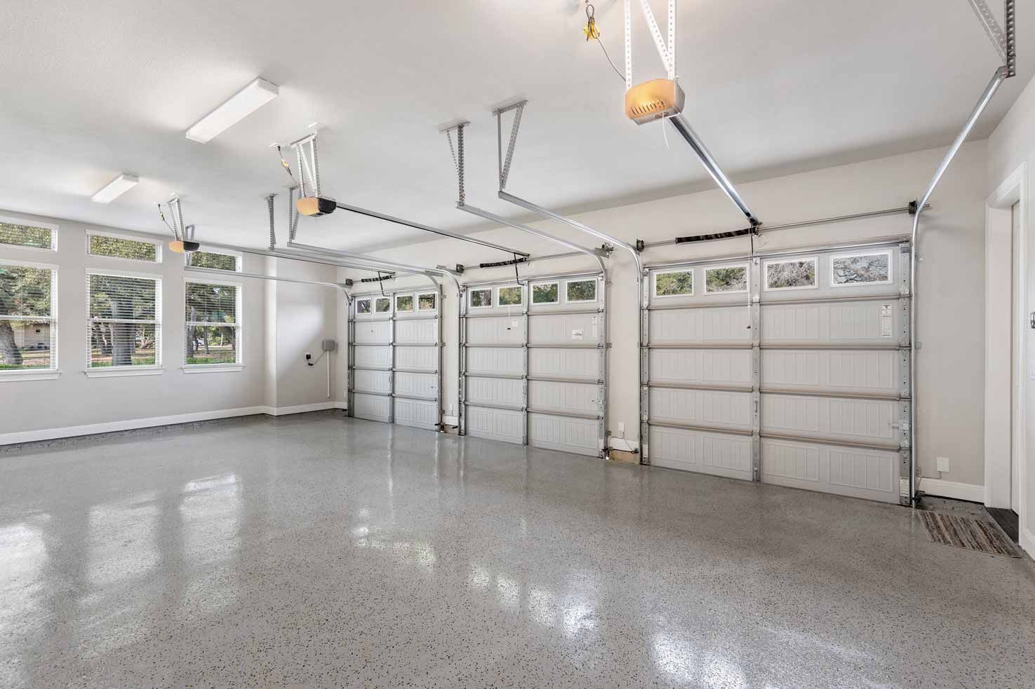 Empty modern garage with three white doors, windows, and polished gray floor