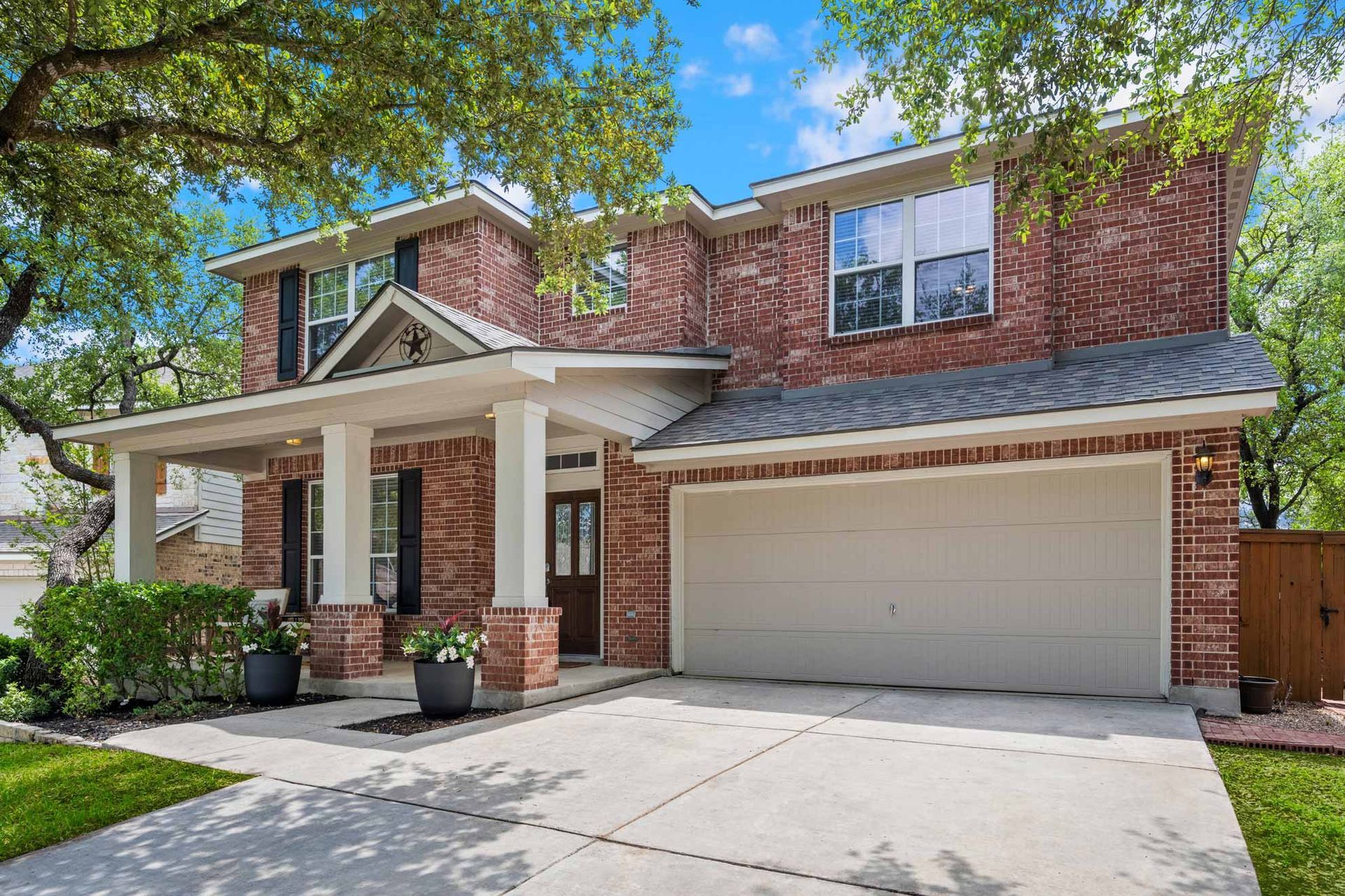 Two-story brick house with white porch columns, two-car garage, and driveway under blue sky