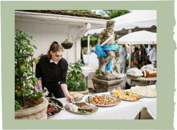 A woman is serving food at a buffet table with a statue in the background.