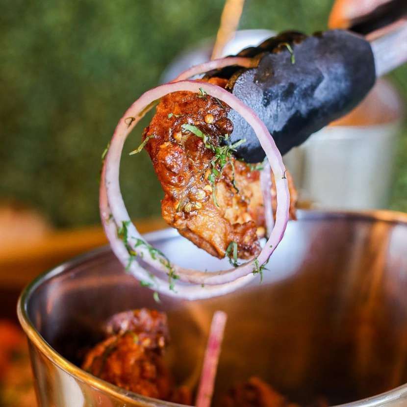 A person is holding a piece of meat with onions in a bucket.