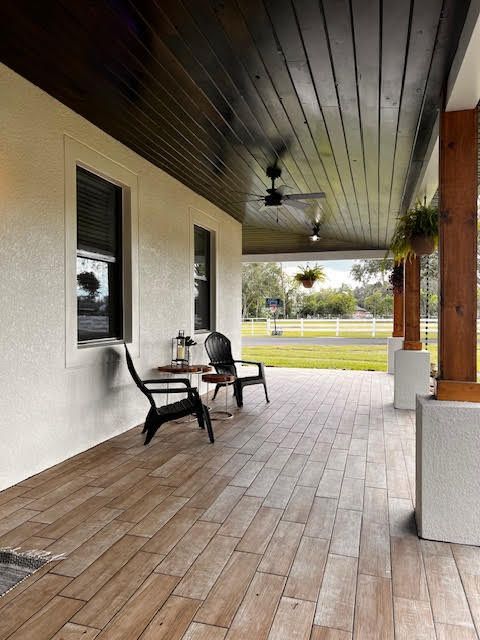 A porch with wooden floors and chairs and a ceiling fan.