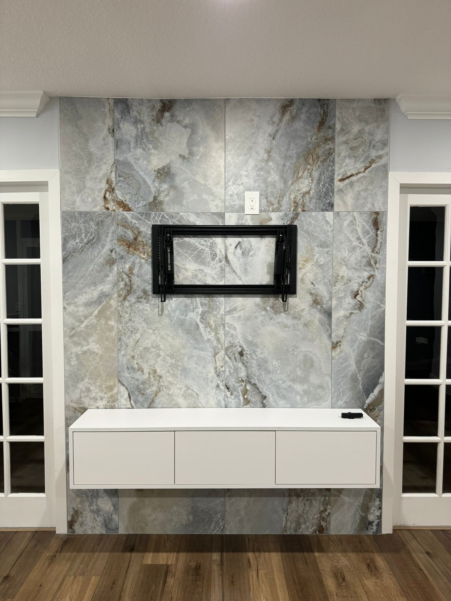 A living room in Palm Beach County with a marble wall and a flat screen tv mounted on it.