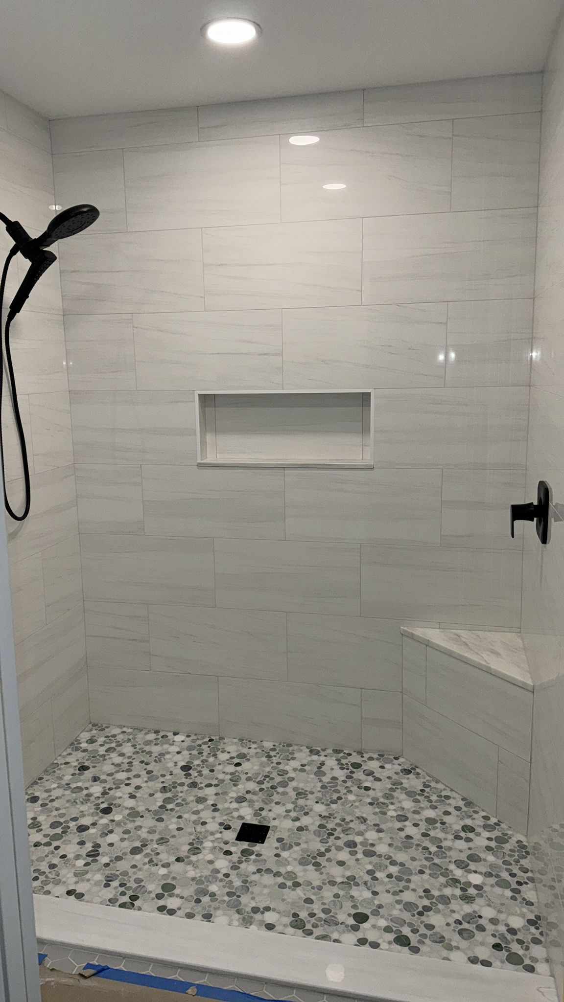 A shower in Palm Beach County with white tiles and a black shower head.