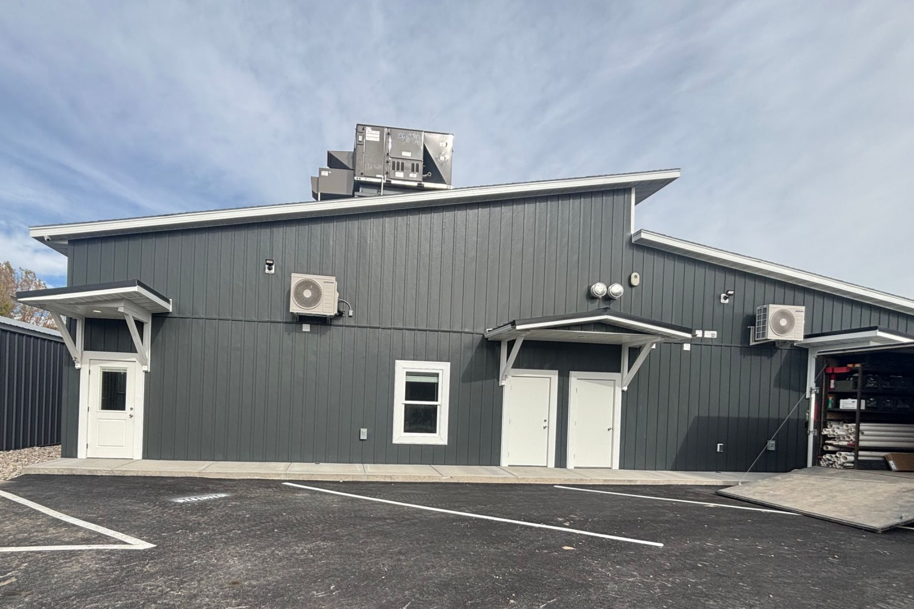 Gray industrial building with white doors and air-conditioning units beside a parking lot