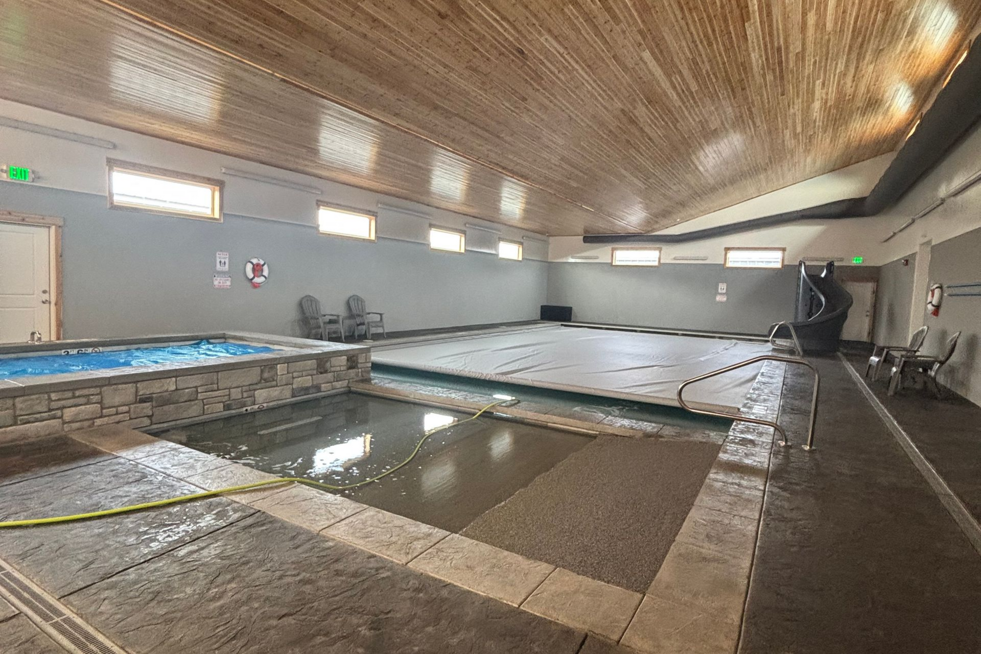 Indoor swimming pool with tiled deck, water jets, and lounge chairs under a wood-paneled ceiling
