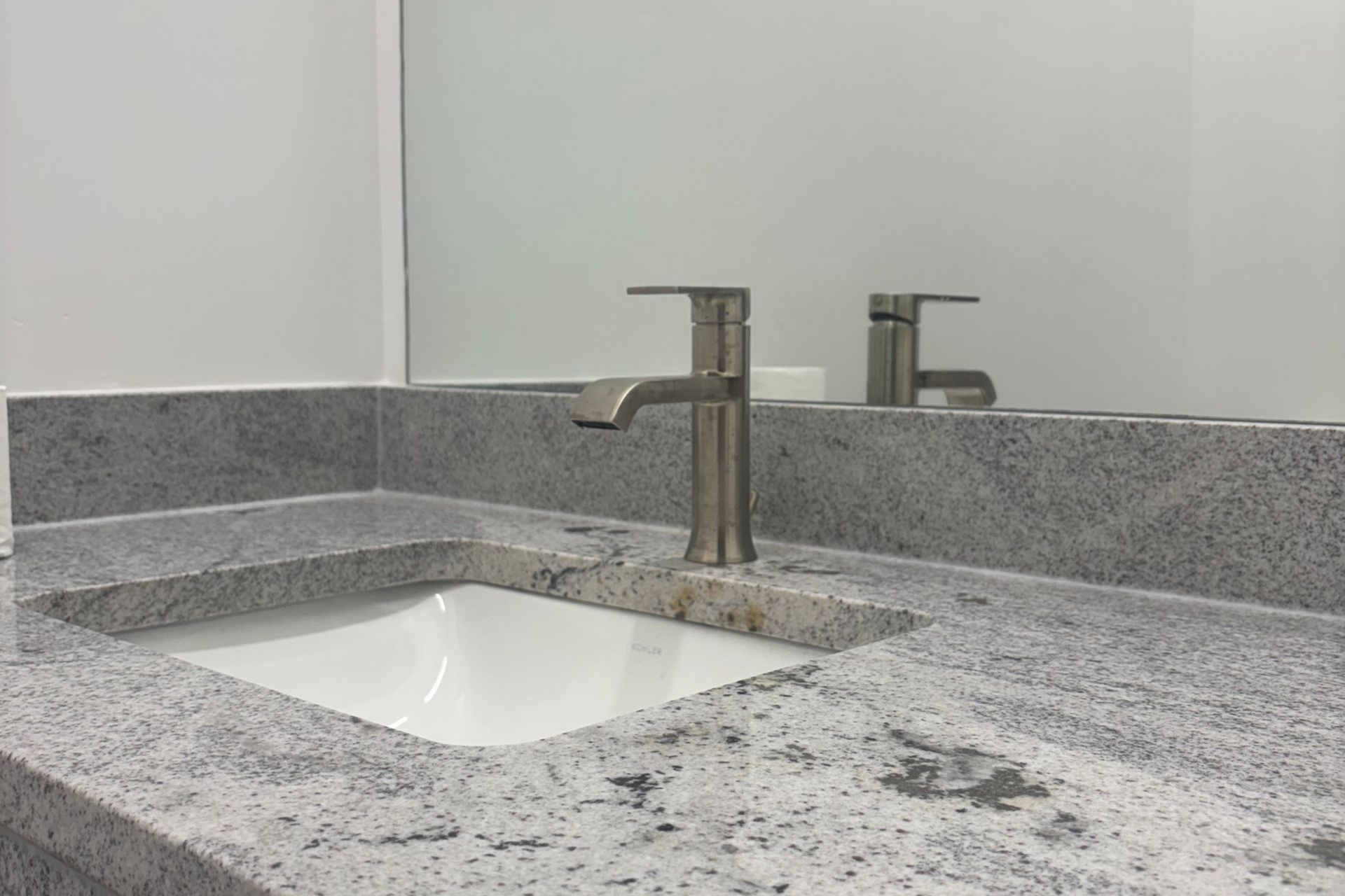 Bathroom vanity with speckled granite countertop, white sink, and chrome faucet reflected in mirror