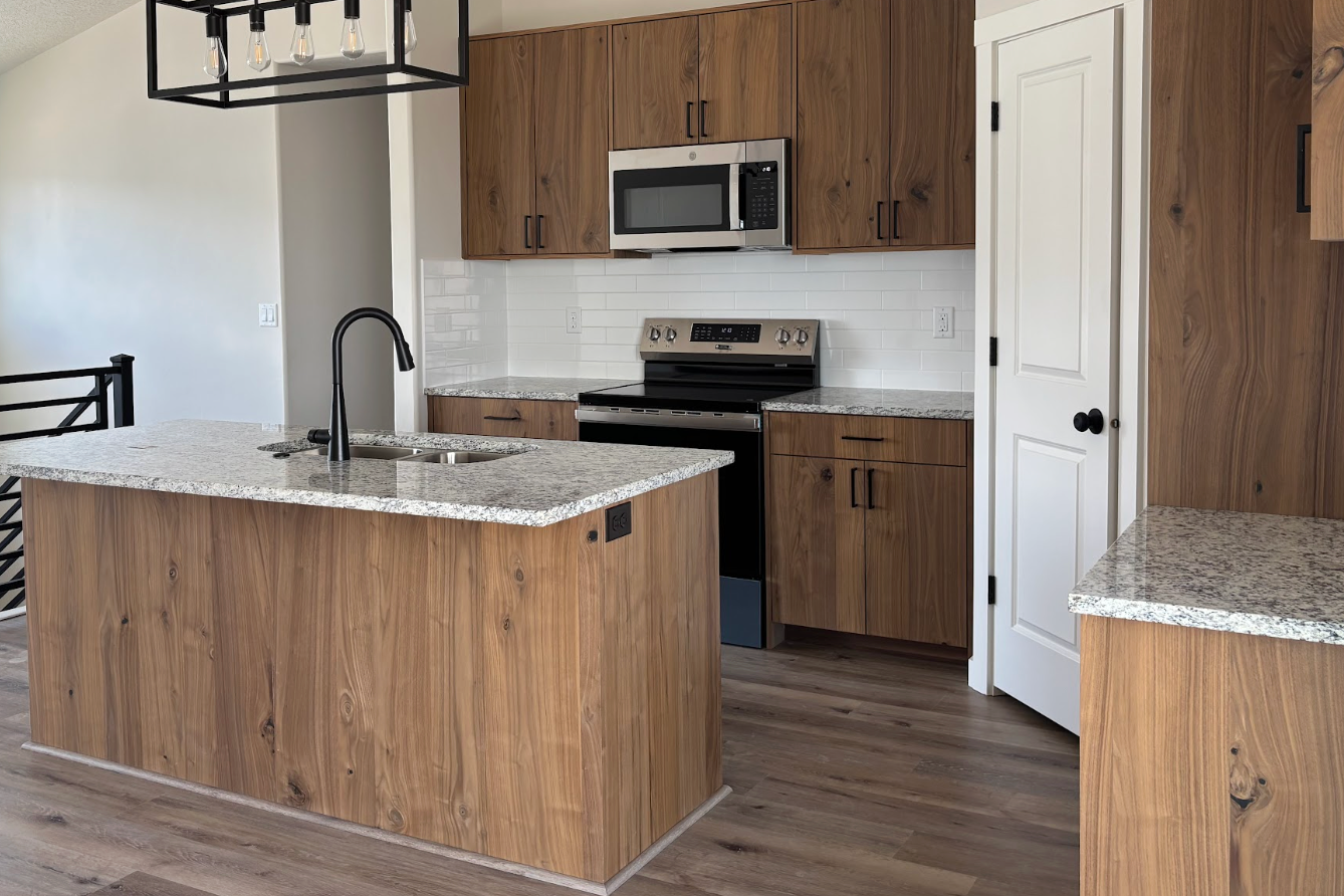 Modern kitchen with wood cabinets, granite island, stainless stove, microwave, and white pantry door