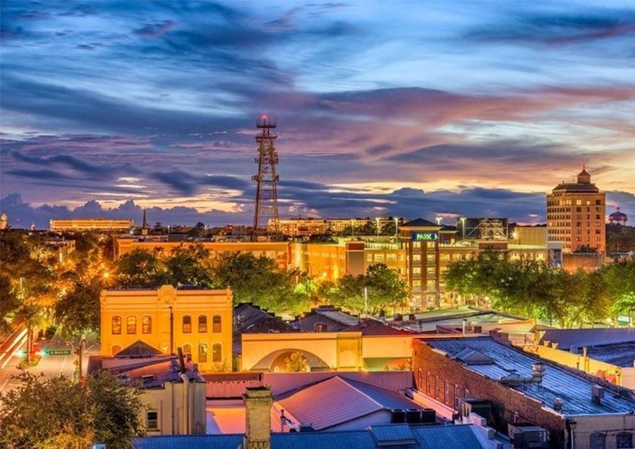 City skyline at dusk with lit buildings, cloudy sky.