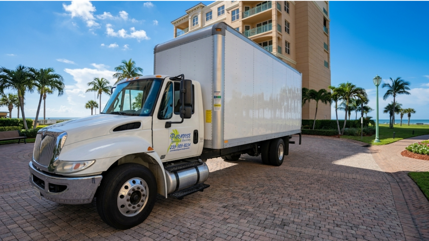 White box truck parked outside a beachfront hotel with palm trees and blue sky in the background