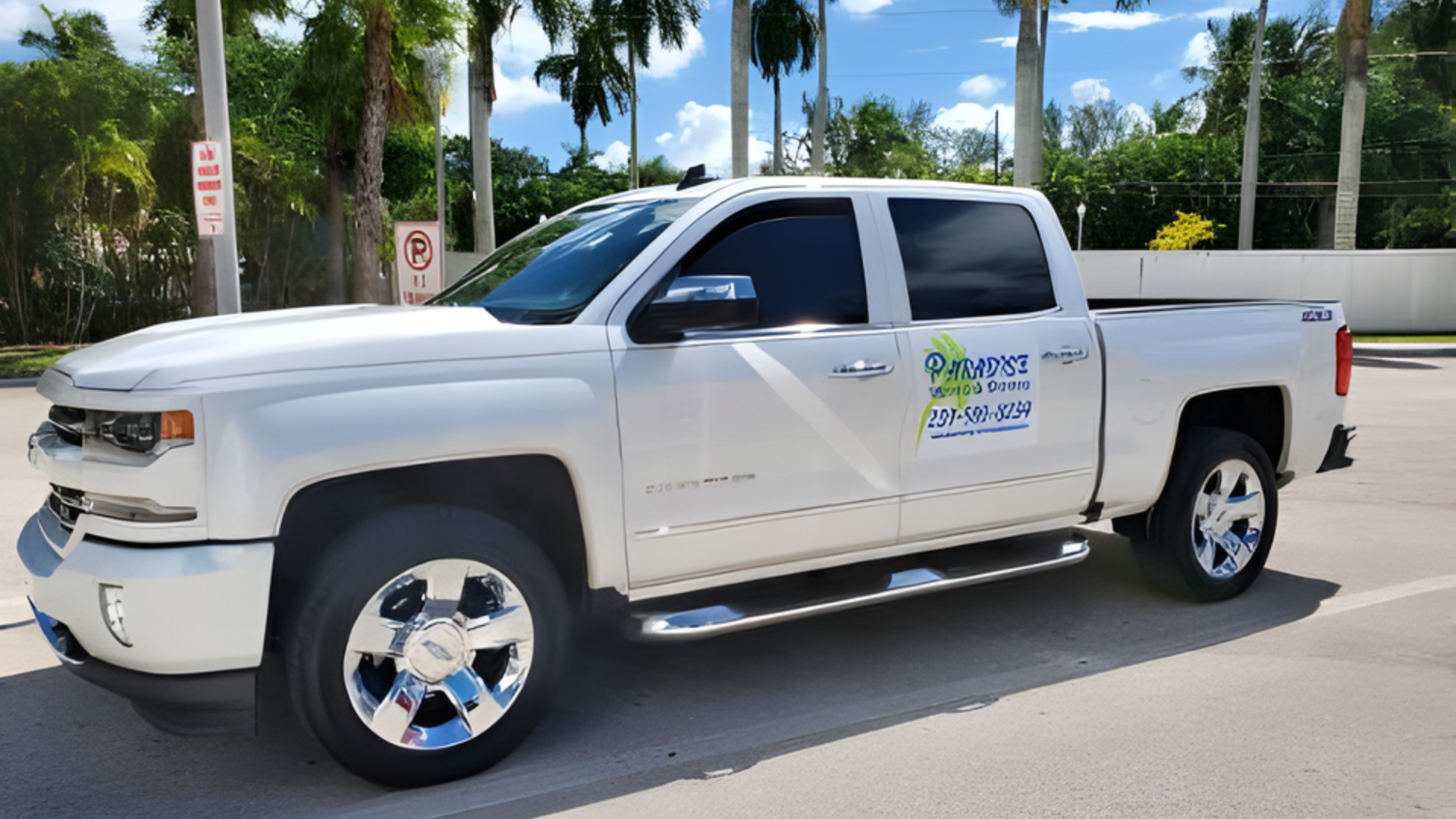 White pickup truck parked on a sunny street with palm trees and a clear blue sky