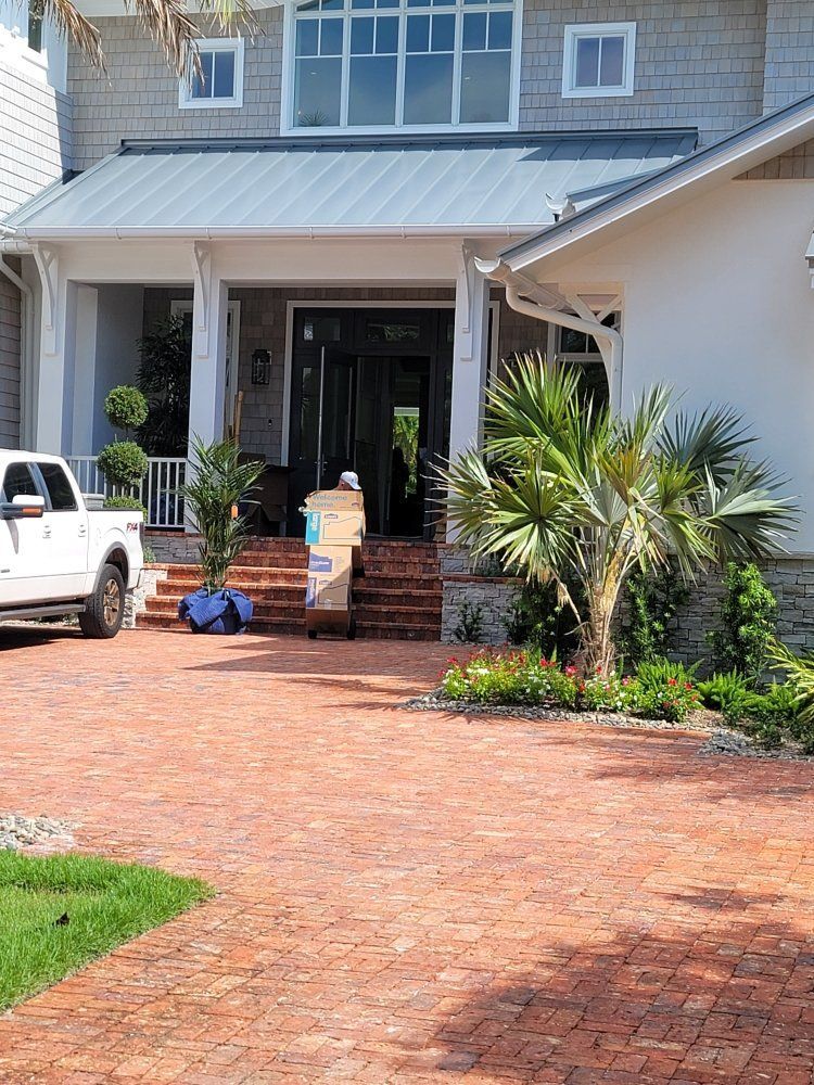 Brick driveway leading to a white house with front porch, potted plants, and a parked white truck