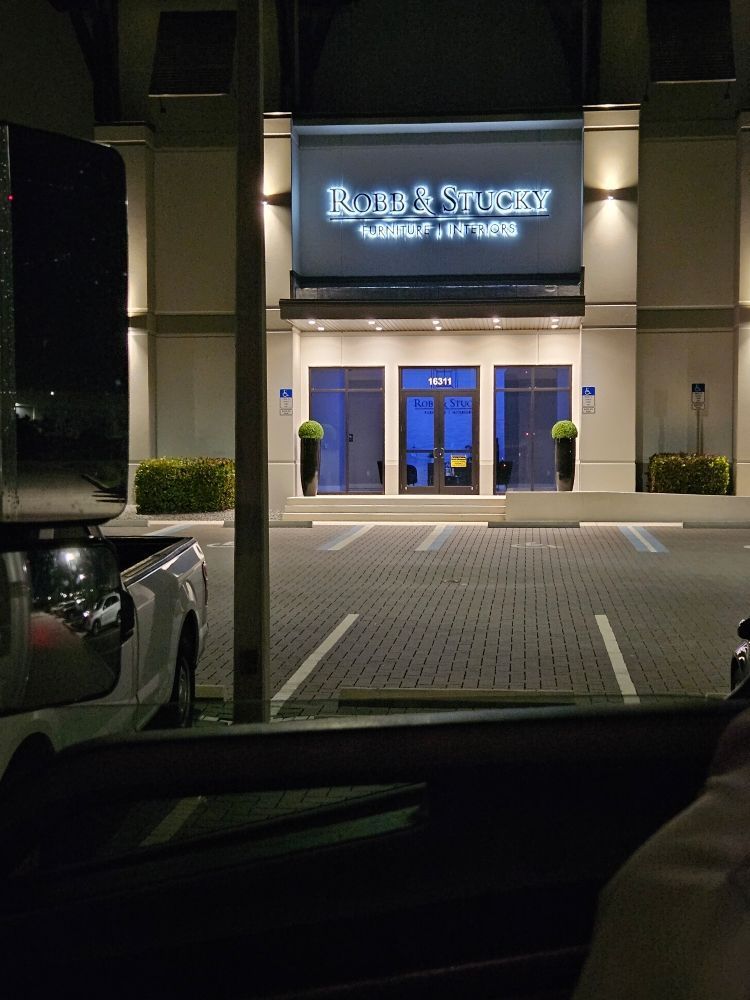 Night view of a storefront entrance with blue doors and illuminated sign above the sidewalk.
