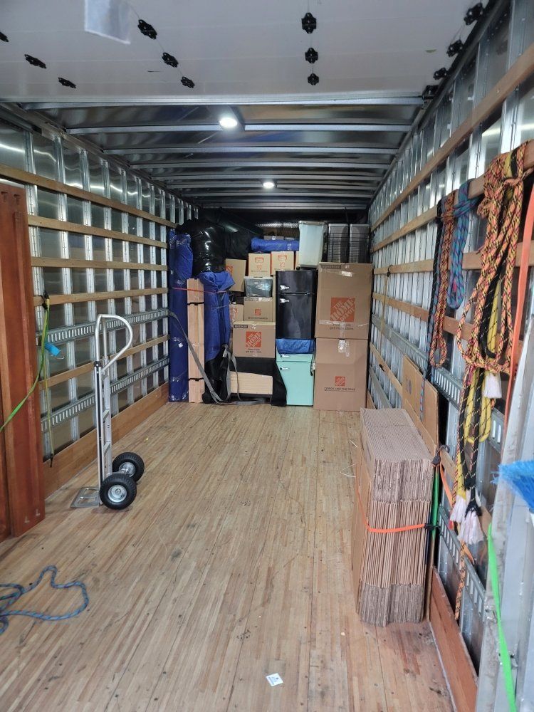 Inside a moving truck with stacked boxes, shelves, and packed supplies along the walls